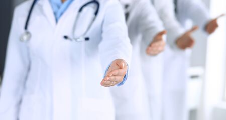 Group of modern doctors standing as a team whole offering helping hand for shaking hand or saving life. Physicians ready to examine and help patients in hospital office. Medical help, insurance in health care, best desease treatment and medicine concept.の写真素材