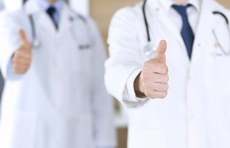 Group of modern doctors standing as a team with thumbs up or Ok sign in hospital office, close-up. Physicians ready to examine and help patients. Medical help, insurance in health care, best treatment and medicine concept.の写真素材
