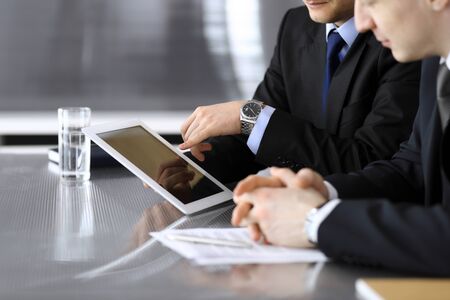 Businessman using tablet computer and work together with his colleague or partner at the glass desk in modern office, close-up. Unknown business people at meeting. Teamwork and partnership concept.の写真素材