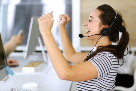 Business woman using headset for communication and consulting people at customer service office. Call center. Group of operators at work at the background. Casual dress styleの写真素材