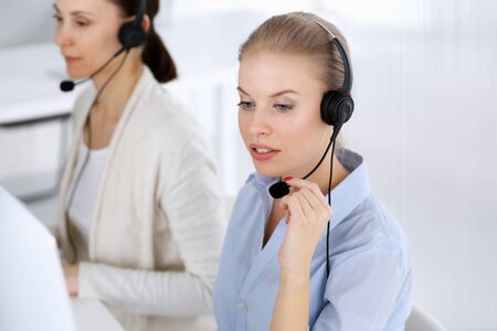 Call center office. Beautiful blonde woman using computer and headset for consulting clients online. Group of operators working as customer service occupation. Business people conceptの写真素材