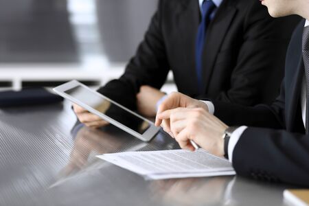 Businessman using tablet computer and work together with his colleague or partner at the glass desk in modern office, close-up. Unknown business people at meeting. Teamwork and partnership conceptの写真素材