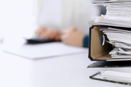 Binders with papers are waiting to be processed by business woman or bookkeeper working at the desk...