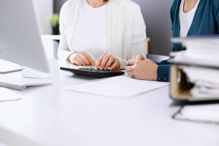 Accountant checking financial statement or counting by calculator income for tax form, hands closeup. Business woman sitting and working with colleague at the desk in office. Tax and Audit conceptの写真素材