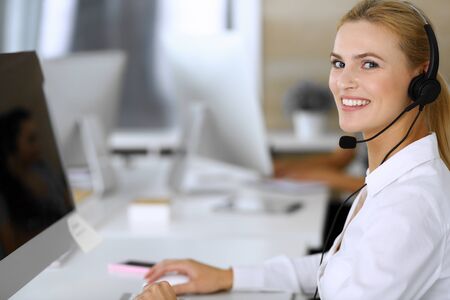 Blonde business woman using headset for communication and consulting people at customer service...