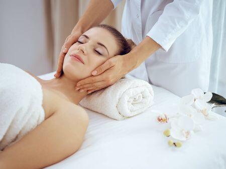 Young and blonde woman enjoying facial massage in spa salon. Beauty conceptの写真素材