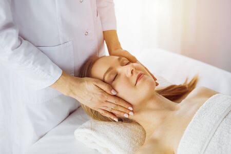 Beautiful caucasian woman enjoying facial massage with closed eyes in spa salon. Relaxing treatment in medicine and Beauty concept.の写真素材