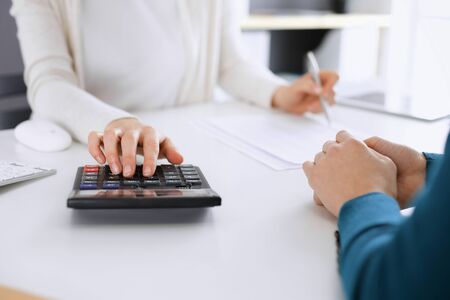 Accountant checking financial statement or counting by calculator income for tax form, hands closeup. Business woman sitting and working with colleague at the desk in office toned in blue. Tax and Audit conceptの写真素材