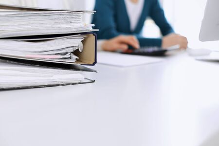 Bnders with papers are waiting to be processed by business woman or bookkeeper working at the desk...