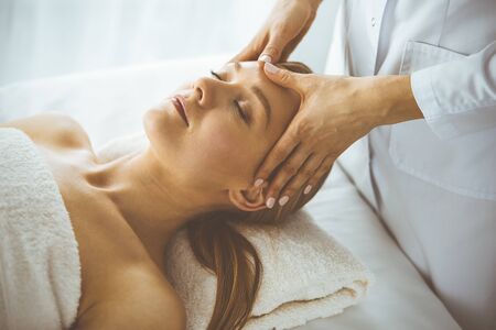 Beautiful happy woman enjoying facial massage with closed eyes in spa salon. Relaxing treatment in medicine and Beauty conceptの写真素材
