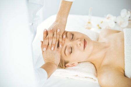 Beautiful happy woman enjoying facial massage with closed eyes in spa salon. Relaxing treatment in medicine and Beauty conceptの写真素材