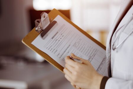 Unknown female doctor using clipboard in sunny clinic. Perfect medical service in hospitalの写真素材