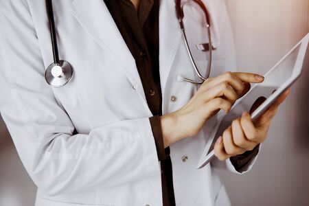Unknown female doctor using tablet computer in sunny clinic. Perfect medical service in hospitalの写真素材