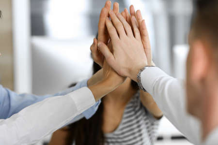 Group of business people joining hands or giving five to each other after meeting or negotiation in...