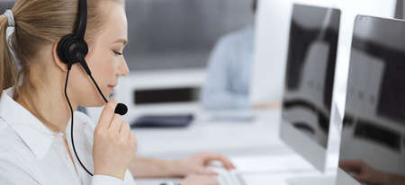Call center. Group of casual dressed operators at work. Blond business woman in headset at customer...