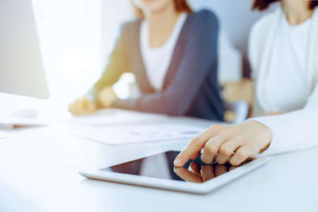 Businesswoman pointing at tablet computer screen while giving presentation to her female colleague. Group of business people working at the desk in office. Teamwork conceptの写真素材
