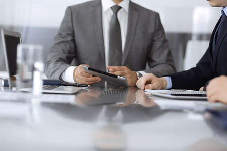 Unknown businessman using tablet computer and working together with his colleague while sits at the glass desk in modern office. Teamwork and partnership conceptの写真素材