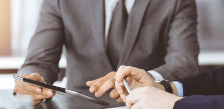 Unknown businessman using tablet computer and working together with his colleague while sits at the glass desk in modern office. Teamwork and partnership conceptの写真素材