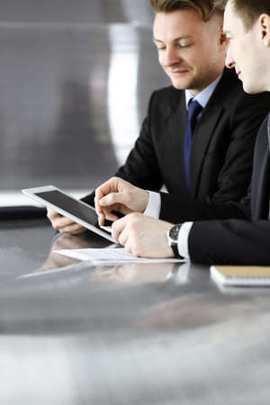 Unknown businessmen using tablet computer and work together at the glass desk in modern office, close-up. Teamwork and partnership conceptの写真素材