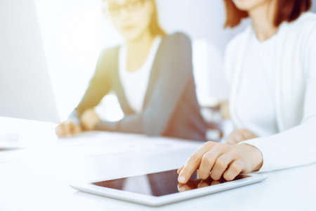 Businesswoman pointing at tablet computer screen while giving presentation to her female colleague. Group of business people working at the desk in office. Teamwork conceptの写真素材