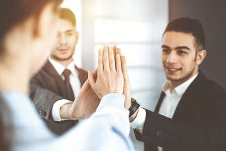 Business people group showing teamwork, joining hands and giving five to each other in sunny office
