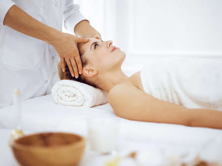 Young and blonde woman enjoying facial massage in spa salon. Beauty conceptの写真素材