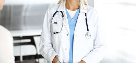Unknown woman-doctor communicating with female patient. Physician checks medical history record and...