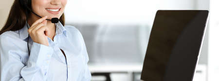 Brunette female customer service representative in a headset is consulting clients online. Call...