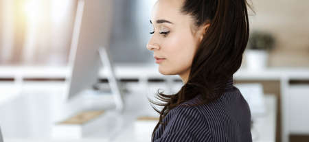 Business woman using computer at workplace in sunny office. Working for pleasure and successの写真素材