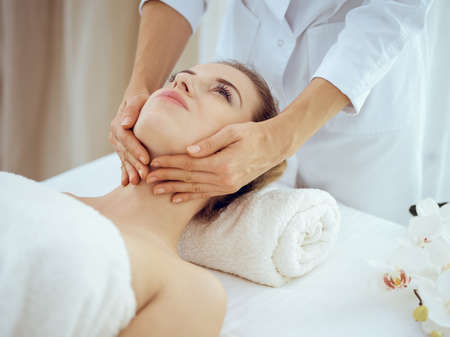 Young and blonde woman enjoying facial massage in spa salon. Beauty conceptの写真素材