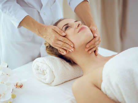 Young and blonde woman enjoying facial massage in spa salon. Beauty conceptの写真素材