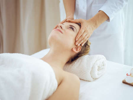 Young and blonde woman enjoying facial massage in spa salon. Beauty conceptの写真素材