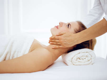 Young and blonde woman enjoying facial massage in spa salon. Beauty conceptの写真素材