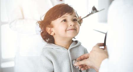 Woman-doctor examining a child patient by stethoscope in sunny clinik. Cute arab toddler at physician appointmentの写真素材