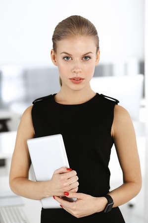 Young blond businesswoman is standing straight in modern office. Business people concept. Black dress do suits to her much at this portraitの写真素材