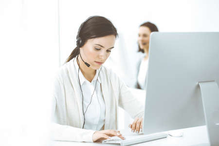 Call center. Casual dressed woman sitting in headset at customer service office. Group of operators at work. Business conceptの写真素材