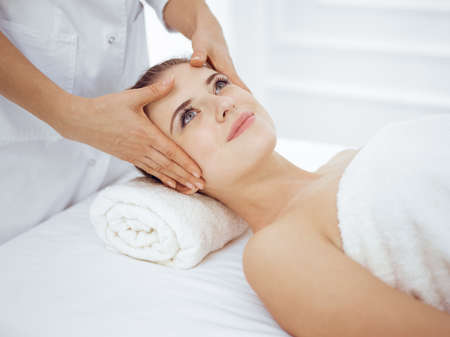 Young and blonde woman enjoying facial massage in spa salon. Beauty conceptの写真素材