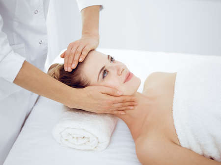 Young and blonde woman enjoying facial massage in spa salon. Beauty conceptの写真素材