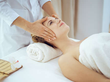 Young and blonde woman enjoying facial massage in spa salon. Beauty conceptの写真素材
