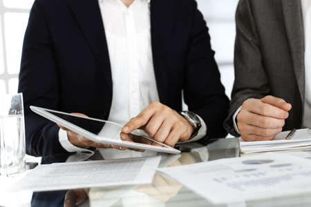 Business people using tablet computer while working together in modern office. Unknown businessman sitting at the desk with his colleague or partner. Teamwork and partnership conceptの写真素材