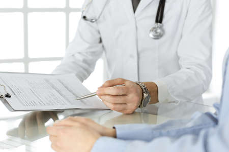 Unknown male doctor and woman-patient discussing current health examination while sitting in clinic...