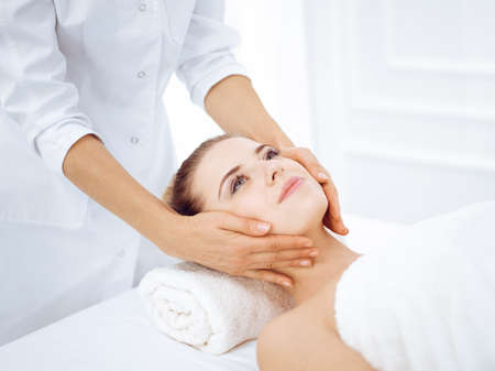 Young and blonde woman enjoying facial massage in spa salon. Beauty conceptの写真素材