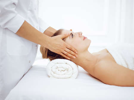 Young and blonde woman enjoying facial massage in spa salon. Beauty conceptの写真素材
