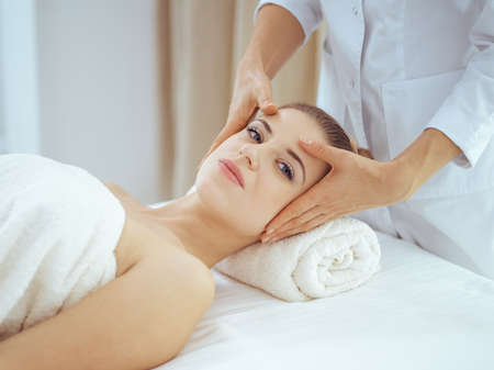 Young and blonde woman enjoying facial massage in spa salon. Beauty conceptの写真素材