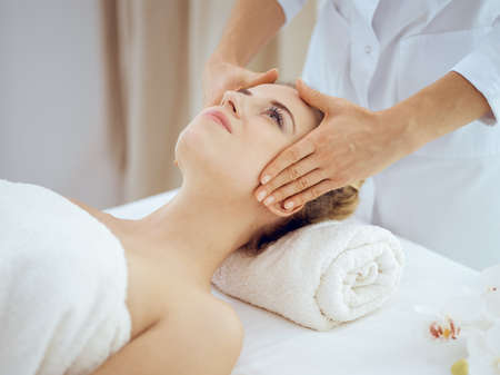 Young and blonde woman enjoying facial massage in spa salon. Beauty conceptの写真素材