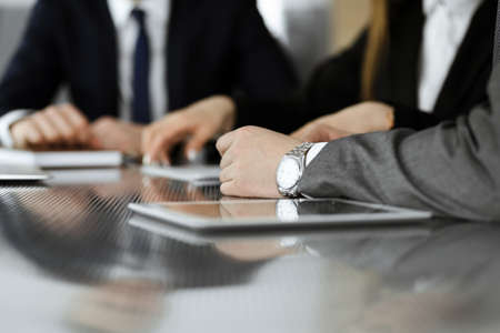 Unknown businessmen and woman sitting, using laptop computer and discussing questions at meeting in...