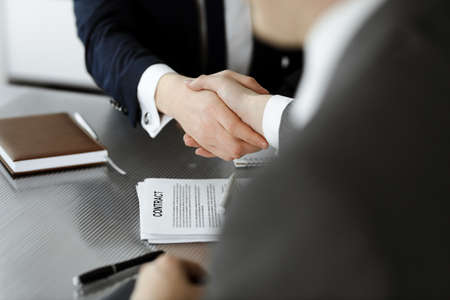 Unknown businessman shaking hands with his colleague or partner above the glass desk in modern...