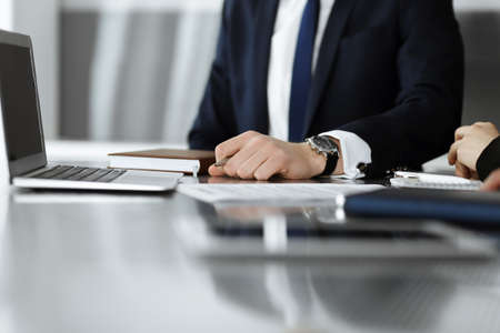 Unknown businessmen and woman sitting, using laptop computer and discussing questions at meeting in...