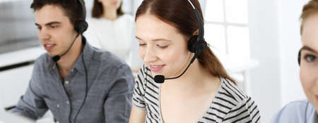 Casual dressed young woman using headset and computer while talking with customers online. Group of operators at work. Call center, business conceptの写真素材