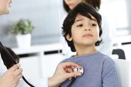 Doctor-woman examining a child patient by stethoscope. Cute arab boy at physician appointment. Medicine conceptの写真素材
